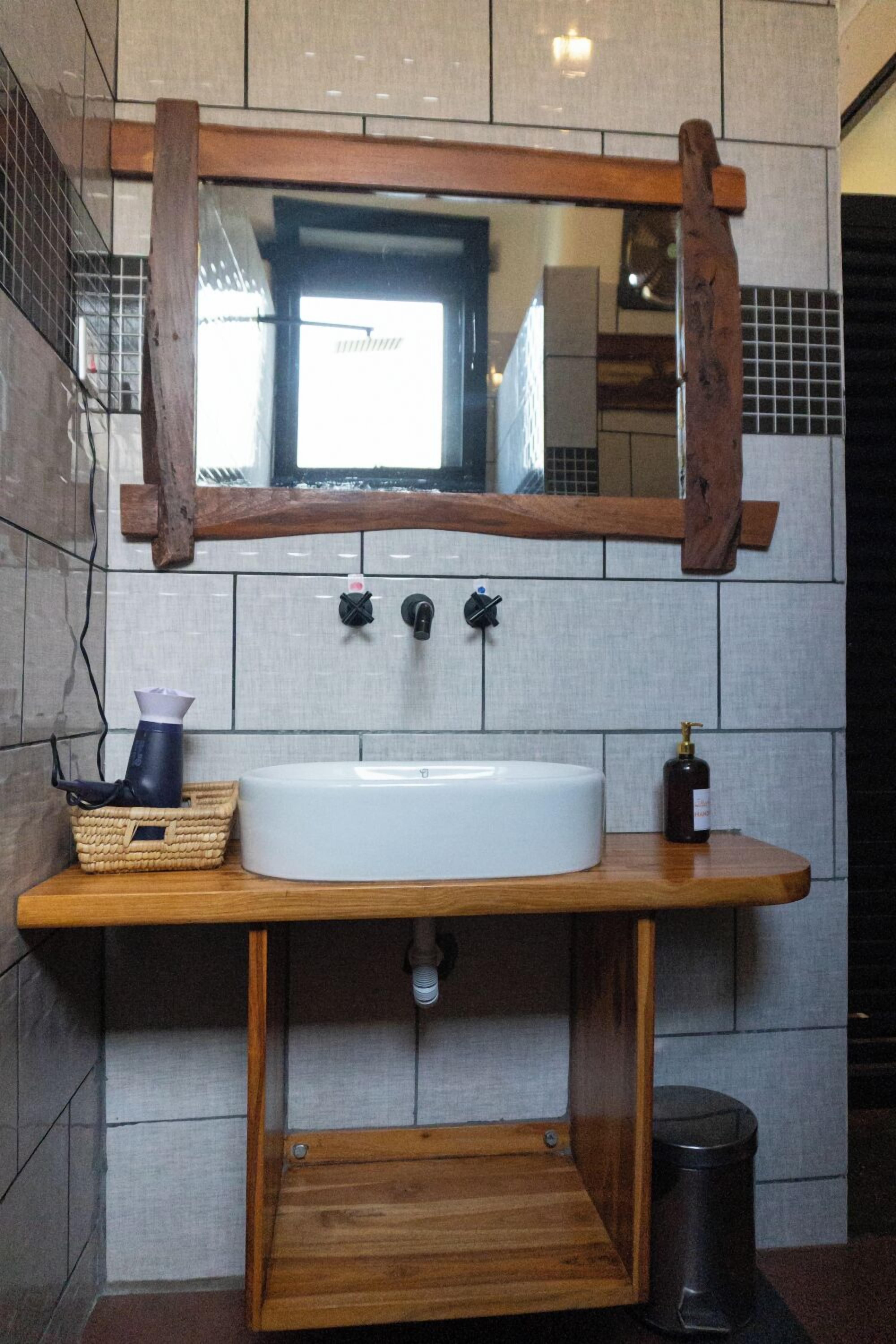 A bathroom with a wooden vanity, a white sink, a mirror, and a trash can.