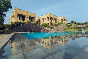 A pool with clear water, surrounded by a stone wall and a building with multiple balconies. - THE MARIDADI HOTEL (Moshi)
