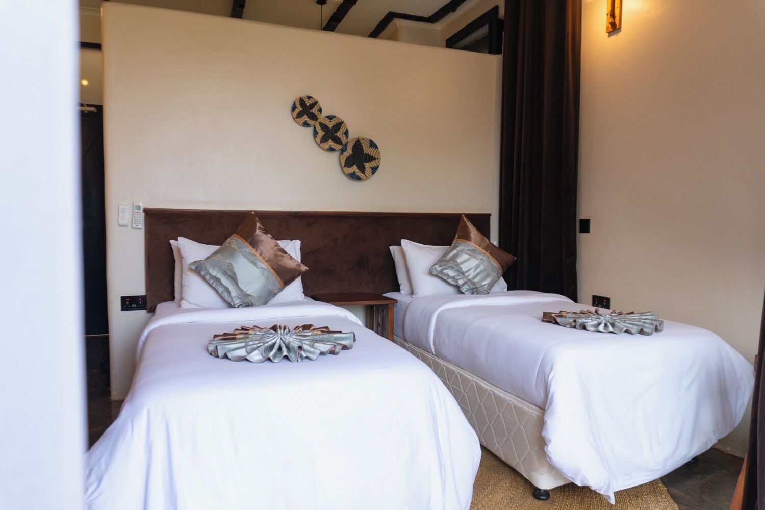 A hotel room with two beds, a wooden headboard, a wall-mounted light fixture, and a telephone.