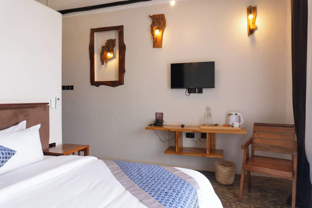 A hotel room with a bed, a TV mounted on the wall, a wooden desk with a coffee maker, and a chair.