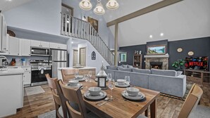 A modern kitchen with white cabinets, a dining table set with plates and glasses, and a grey sofa in the living area. - Hot Tub Chalet, Fire Pit, Lake Access, Dogs OK (Blakeslee)