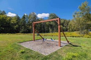 A swing set in a grassy area with trees in the background.
