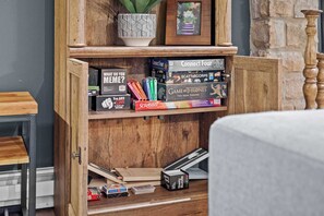 A wooden cabinet with shelves holding board games like Connect Four, Scrabble, and Game of Thrones.