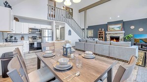 A spacious living area with a dining table set for six, a grey sofa, and a staircase leading to an upper level. - Hot Tub Chalet, Fire Pit, Lake Access, Dogs OK (Blakeslee)
