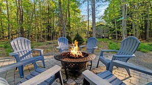 A fire pit with four Adirondack chairs arranged around it in a forested area. - Hot Tub Chalet, Fire Pit, Lake Access, Dogs OK (Blakeslee)