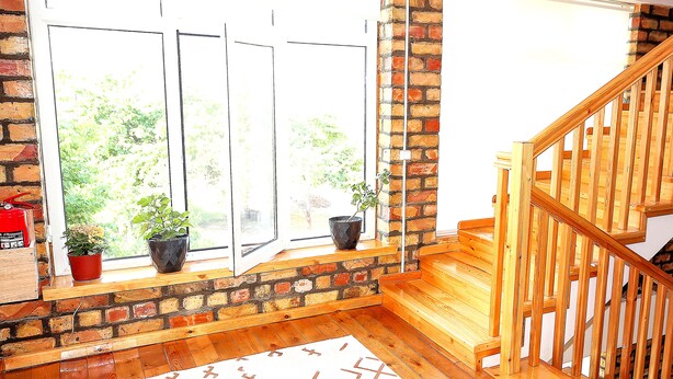 Ein Zimmer mit Holzboden, einem weißen Teppich mit geometrischem Muster, einer Ziegelwand und einer Holztreppe mit Geländer.