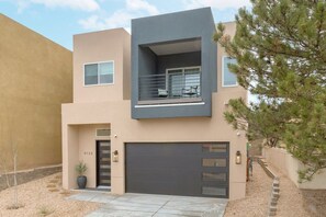 A modern two-story building with a balcony, a garage, and a small tree in the foreground. - The Q by Velo - Stylish Mid-Century Modern Home (Albuquerque)