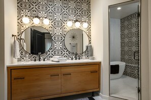 A bathroom with a wooden vanity, two round mirrors, and a patterned wall. - The Q by Velo - Stylish Mid-Century Modern Home (Albuquerque)