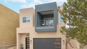 Un bâtiment moderne à deux étages, doté d’un balcon, d’un garage et d’un petit arbre au premier plan.