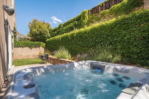 A hot tub in a backyard with a brick wall, a lawn, and a hedge. - The Q by Velo - Stylish Mid-Century Modern Home (Albuquerque)