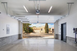 A garage with a concrete floor, a black door, and a ceiling-mounted projector. - The Q by Velo - Stylish Mid-Century Modern Home (Albuquerque)