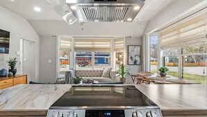 A modern kitchen with a central island, a built-in stovetop, and a large window offering a view of the street.
