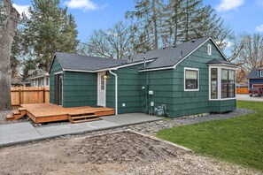 Une maison verte d’un seul étage, dotée d’un porche abrité, d’un petit garage attenant et d’un espace extérieur visible, aménagé pour les équipements techniques.