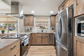 A modern kitchen with wooden cabinets, stainless steel appliances, and a view through the window. - Harrison Haven by Velo in the North End (Boise)