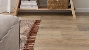 Een woonkamer met een flatscreen televisie aan de muur, een houten console en decoratieve objecten, en een geweven mand eronder.