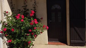 Ein Gebäude mit einer dunklen Holztür und einer kleinen Veranda mit roten Blüten.