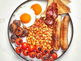 Un plato de comida para el desayuno con huevos, tocino, salchichas, frijoles, champiñones y tomates.