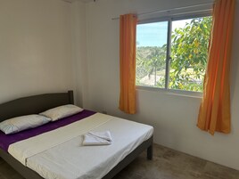 Una cama individual con cabecera, una ventana con cortinas y vistas al exterior.