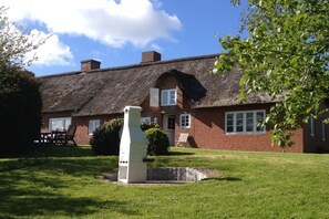 Una casa tradicional de ladrillo con techo de paja, una chimenea blanca y un césped bien cuidado.