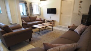 A living room with brown sofas, a coffee table, a flat-screen TV, and a door with a decorative wall hanging. - Holiday home Ockholm (Ockholm)