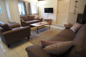A living room with brown sofas, a coffee table, a flat-screen TV, and a door with a decorative wall hanging. - Holiday home Ockholm (Ockholm)