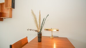 Une table de salle à manger en bois, ornée d’un vase contenant des plantes séchées et d’une lampe de bureau dorée.