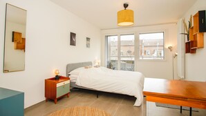 Une chambre à coucher avec un lit, une table de chevet, une lampe et une vue sur l’extérieur par une fenêtre.
