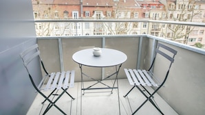Un balcon avec une table ronde et deux chaises, donnant sur une rangée d’immeubles.