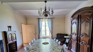 Een eetkamer met een grote ronde tafel, stoelen, een kroonluchter en een kast.