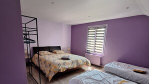 Een slaapkamer met twee bedden, een stapelbed, houten vloeren, een raam met zonwering en een radiator.