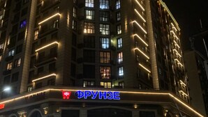 A multi-story building with illuminated signage reading "ФРУНЗЕ" and "24/7" indicating a 24-hour service. - Mountain view, city view, nice terrace, 5 min walking from malls, security 24/7 (Bishkek)