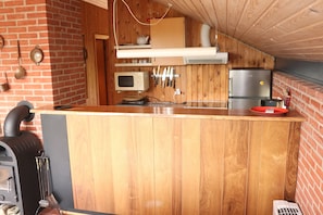 A kitchen with a brick wall, wooden cabinets, a microwave, knives, a toaster, and a refrigerator.