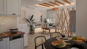 Une cuisine moderne avec des meubles blancs, un coin repas doté d’une table ronde et un espace détente avec un canapé et une fenêtre équipée de stores.