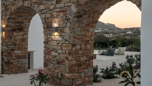 Un arc en pierre mène à un espace de détente agrémenté de coussins et offrant une vue sur un paysage lointain.