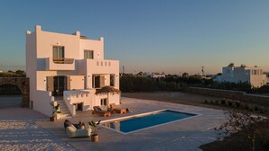 Une villa moderne aux murs blancs, dotée d’une piscine, d’un espace salon extérieur et offrant une vue sur le paysage environnant.