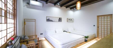 A room with two beds, a wooden bench, a small table, and a window with a view.