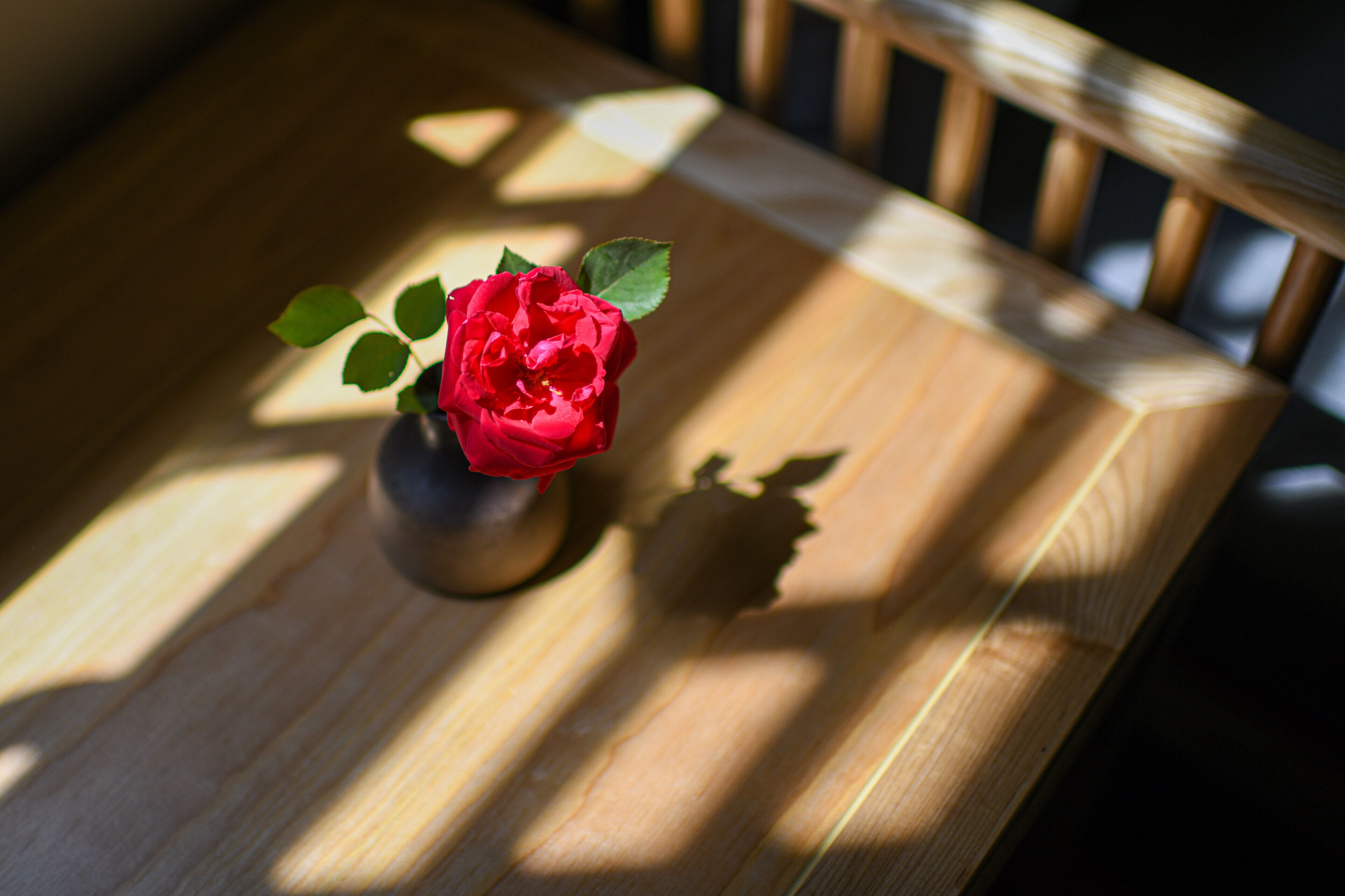 A wooden table with a vase containing a red flower.