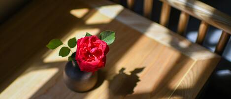 A wooden table with a vase containing a red flower.