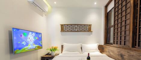 A hotel room with a bed, a TV on the wall, a window with a wooden frame, and a tray with wine glasses and a bottle.