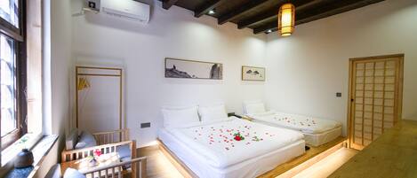 A hotel room with two beds, a wooden bench, a small table, and a window with a view.