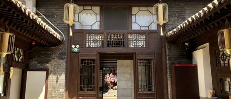 A traditional building with a tiled roof, wooden doors, and a small garden area with potted plants.