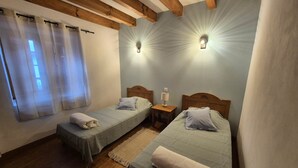 Een slaapkamer met twee eenpersoonsbedden, houten balken aan het plafond en twee wandlampen.