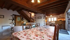 Een ruime eetruimte met een lange tafel, houten stoelen, een trap en een keuken met stenen muren.