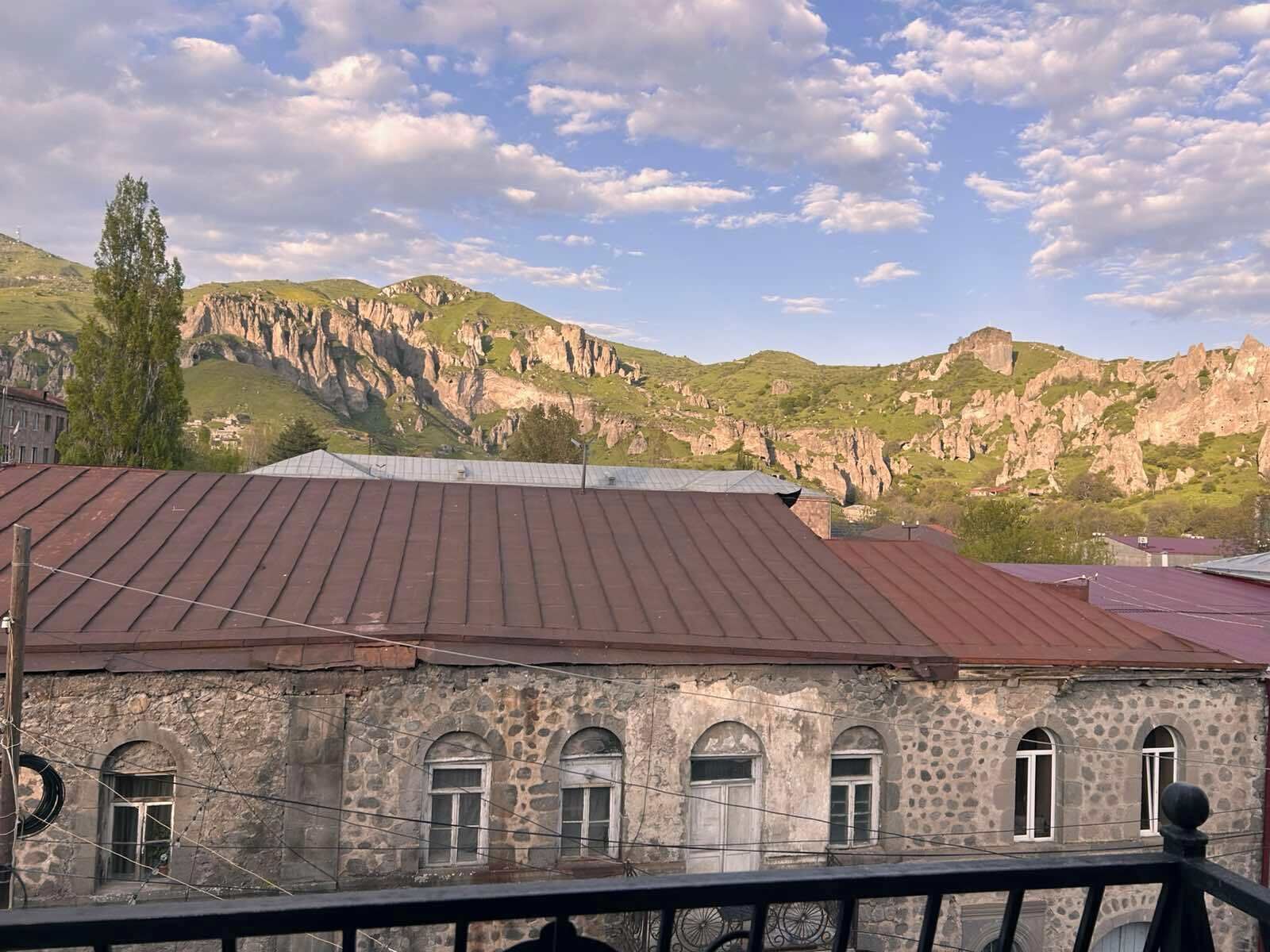 Un edificio con fachada de piedra y ventanas arqueadas, situado frente a un paisaje montañoso con riscos rocosos.
