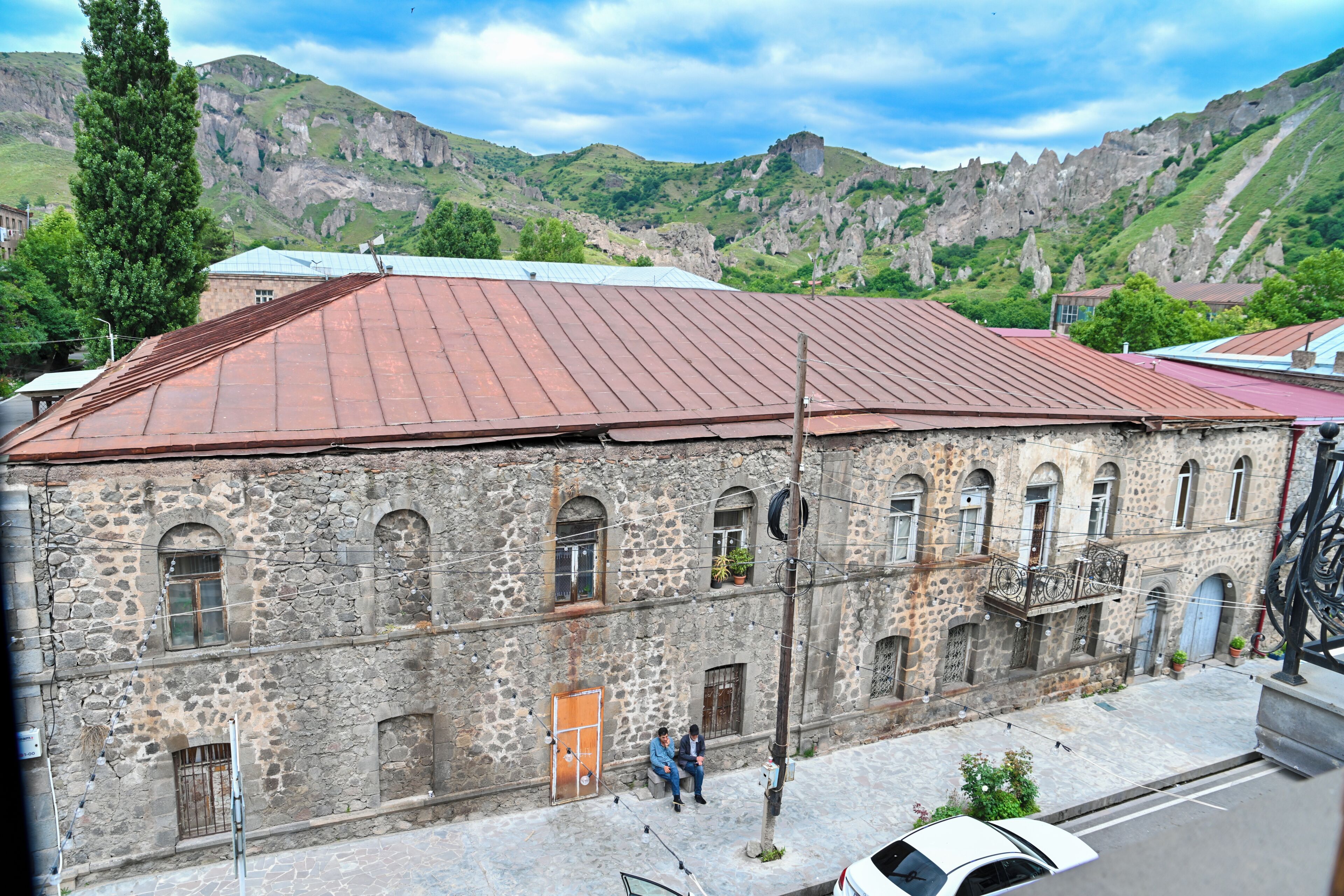 A stone building with a red roof, multiple windows, and a street in front.