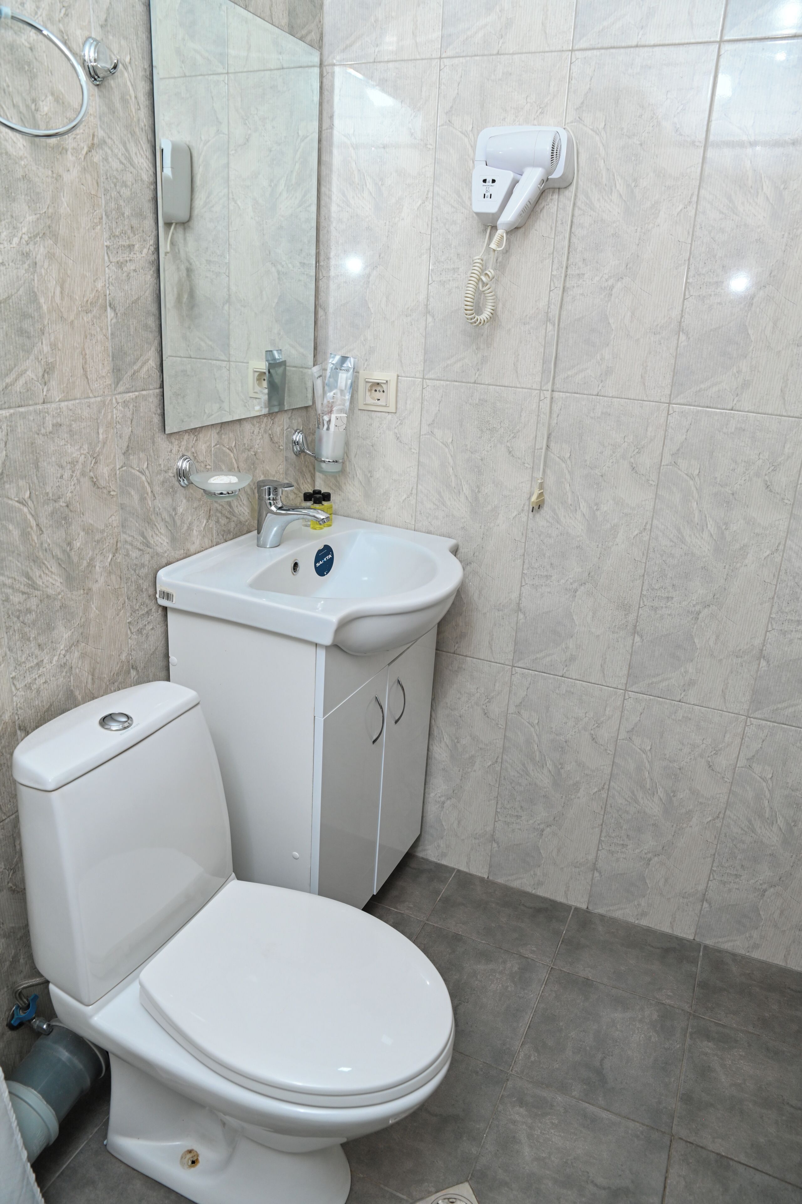A bathroom with a toilet, sink, mirror, and hairdryer on the wall.