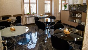 A modern dining area with round tables, black chairs, and a kitchen area with appliances. - Har-Mar Hotel (Goris)