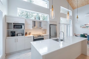 Une cuisine moderne avec des meubles blancs, un grand îlot central, des appareils en acier inoxydable et des luminaires suspendus.