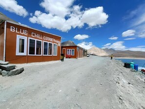 Ein Gebäude mit der Aufschrift "Blue Chill Cottage", umgeben von Erde und mit Bergen im Hintergrund.