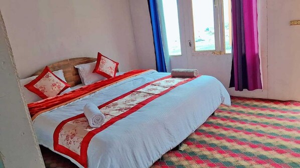 A neatly made bed with a red and white bedspread, pillows, and a rolled towel. The room has a checkered floor and a window with curtains. - Blue Chill Cottage Pangong (Leh)